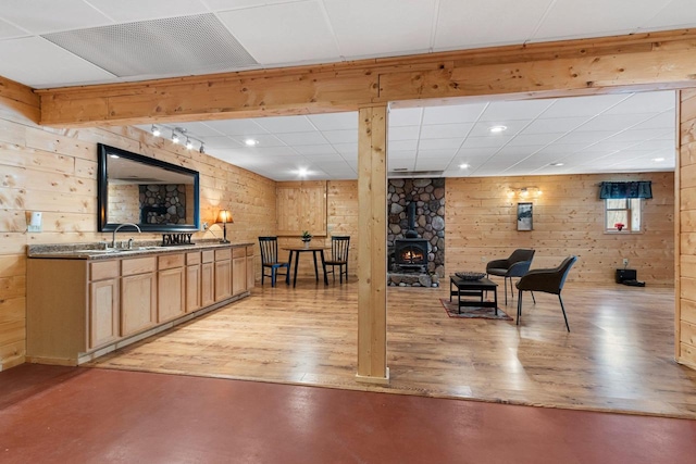 interior space featuring wooden walls, light wood-type flooring, a drop ceiling, light brown cabinets, and sink