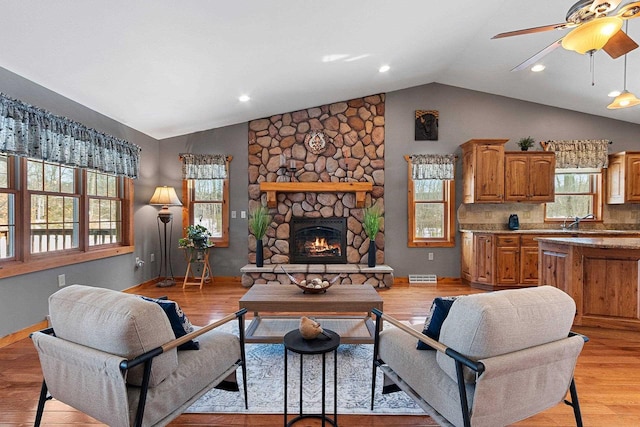 living room with light hardwood / wood-style floors, vaulted ceiling, ceiling fan, and a fireplace