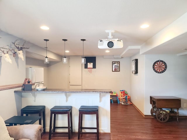 kitchen with kitchen peninsula, decorative light fixtures, white fridge, dark wood-type flooring, and a breakfast bar area