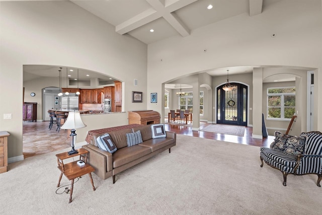 living room with a notable chandelier, light colored carpet, a high ceiling, and beam ceiling