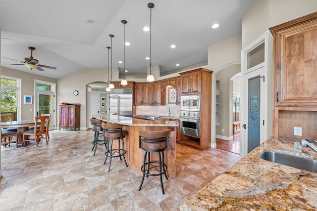 kitchen featuring built in appliances, sink, light stone counters, decorative light fixtures, and a spacious island