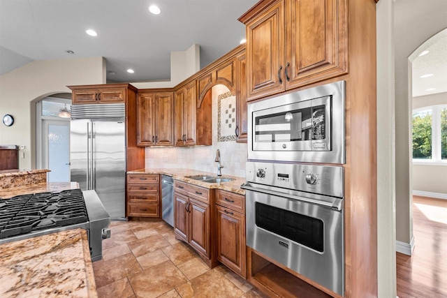 kitchen featuring built in appliances, sink, light stone countertops, and backsplash