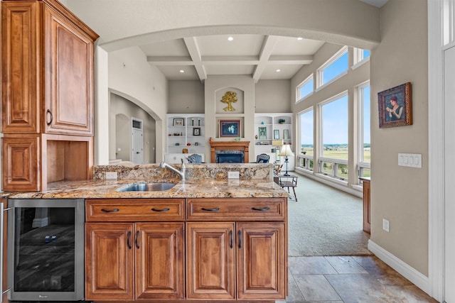 kitchen with wine cooler, sink, light stone counters, coffered ceiling, and beamed ceiling