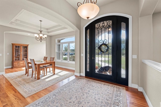 foyer with a raised ceiling, light hardwood / wood-style floors, and a notable chandelier