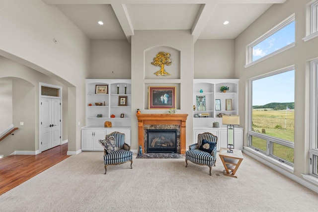 sitting room with beam ceiling, light carpet, a towering ceiling, and a premium fireplace