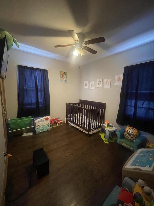 bedroom featuring a crib, hardwood / wood-style flooring, and ceiling fan