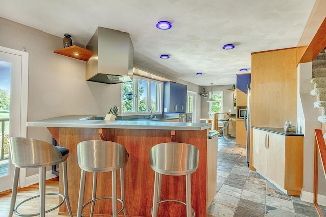 kitchen featuring stainless steel microwave, island range hood, a breakfast bar, sink, and kitchen peninsula