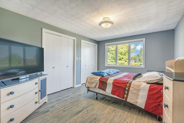 bedroom with a textured ceiling, hardwood / wood-style flooring, and two closets