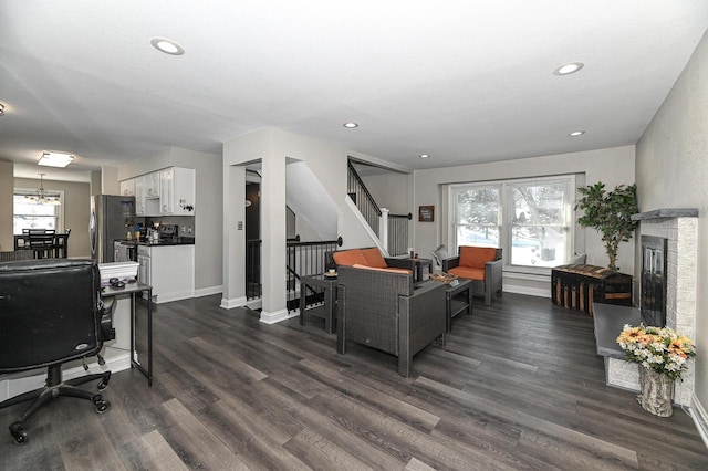 living room with dark hardwood / wood-style flooring, a brick fireplace, and a notable chandelier