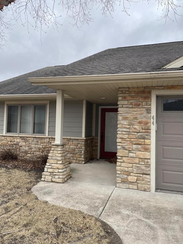 doorway to property with a porch, stone siding, roof with shingles, and a garage