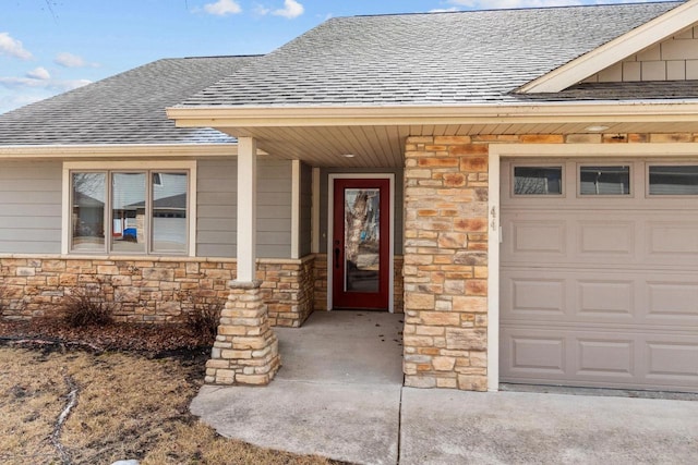 entrance to property featuring a garage, stone siding, and roof with shingles