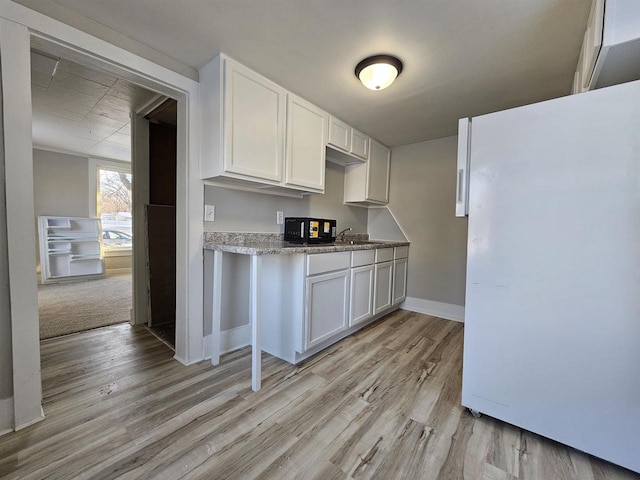 kitchen with white cabinets, white fridge, sink, and light hardwood / wood-style flooring