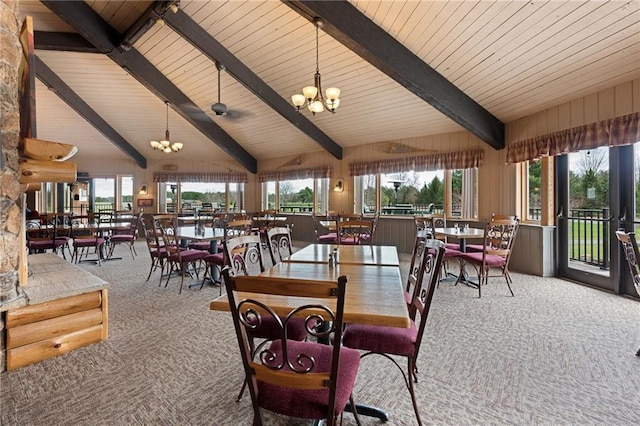 dining space featuring carpet, wood walls, a notable chandelier, and beam ceiling