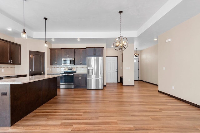 kitchen featuring dark brown cabinetry, stainless steel appliances, a raised ceiling, and hanging light fixtures