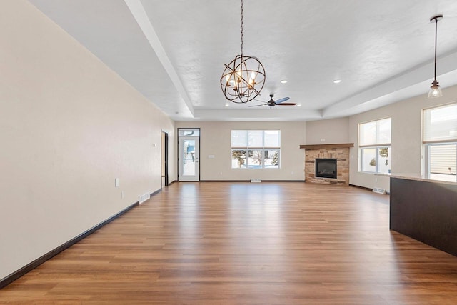 unfurnished living room featuring a stone fireplace, a raised ceiling, wood-type flooring, and a healthy amount of sunlight