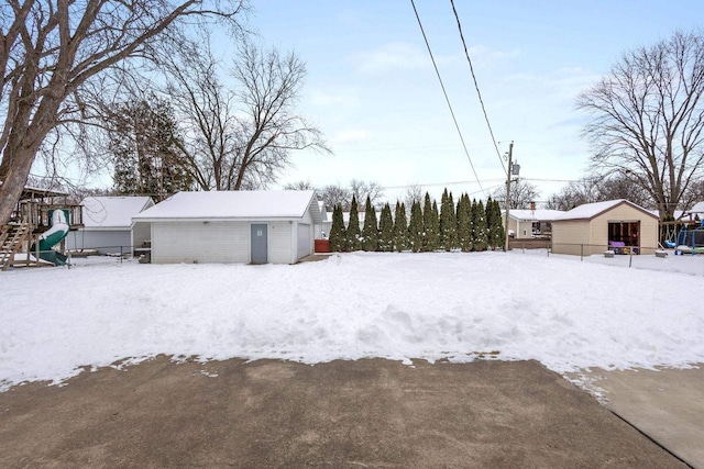 yard covered in snow featuring a playground, an outbuilding, and a garage