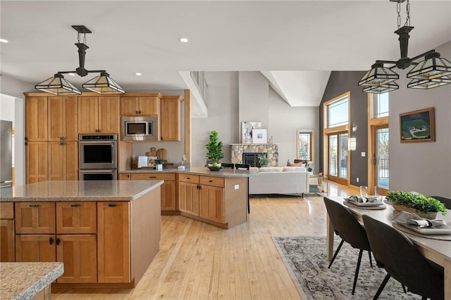 kitchen featuring light hardwood / wood-style flooring, appliances with stainless steel finishes, pendant lighting, a kitchen island, and a stone fireplace