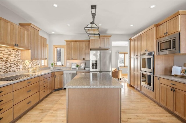 kitchen featuring hanging light fixtures, light wood-type flooring, stainless steel appliances, a kitchen island, and sink