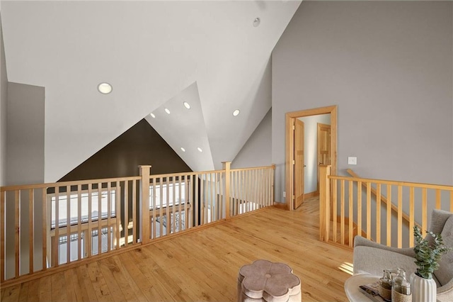 corridor with high vaulted ceiling and light hardwood / wood-style flooring