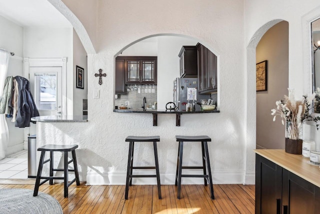 kitchen featuring stainless steel refrigerator, light wood-type flooring, dark brown cabinetry, and a kitchen breakfast bar