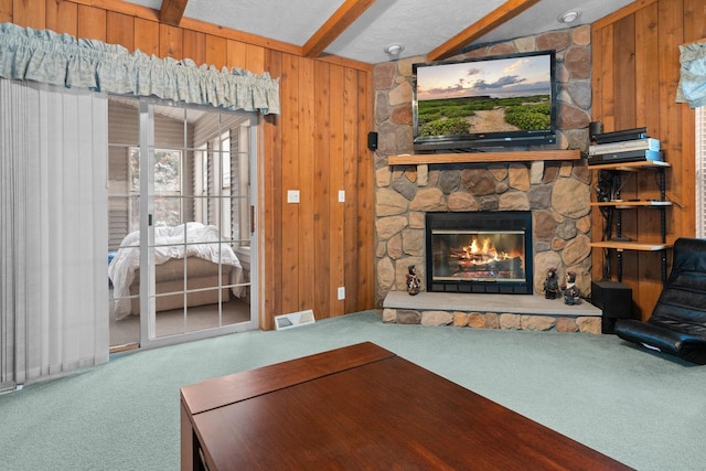 carpeted living room with beamed ceiling, wood walls, and a stone fireplace