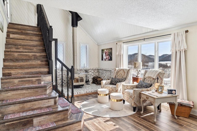 living area featuring lofted ceiling, stairway, wood finished floors, and a wood stove