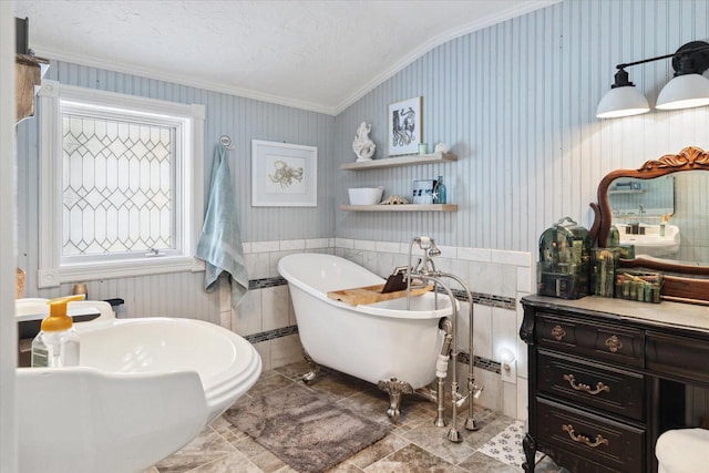 bathroom featuring wallpapered walls, wainscoting, a freestanding tub, and vaulted ceiling