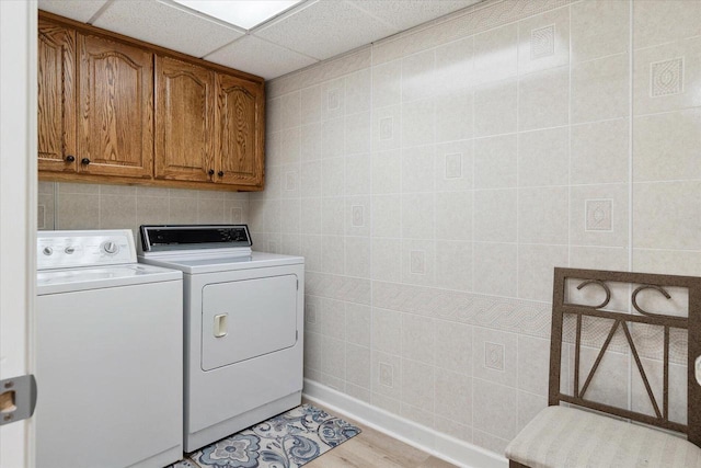 laundry area with tile walls, washing machine and dryer, light wood-style floors, and cabinet space