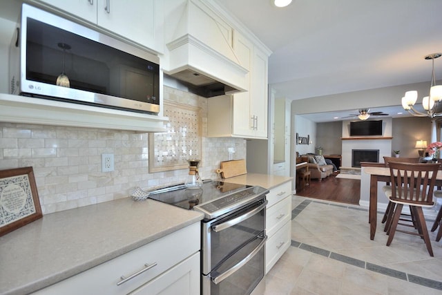 kitchen featuring stainless steel appliances, custom range hood, decorative backsplash, ceiling fan with notable chandelier, and white cabinetry