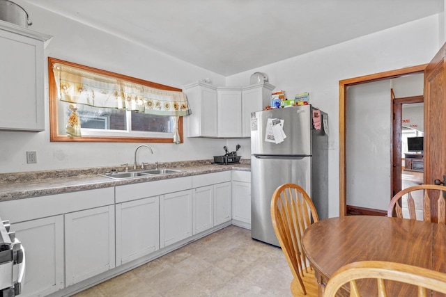 kitchen with sink, range, stainless steel refrigerator, and white cabinets