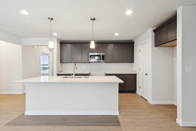 kitchen featuring sink, light wood-type flooring, decorative light fixtures, dark brown cabinetry, and a kitchen island with sink