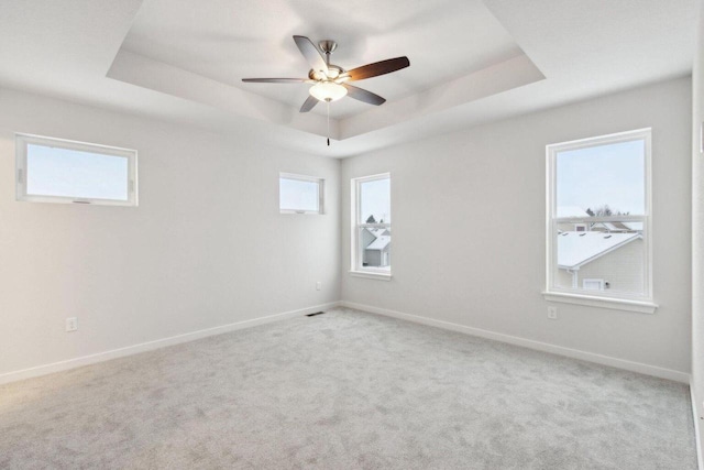 carpeted spare room featuring a tray ceiling and ceiling fan