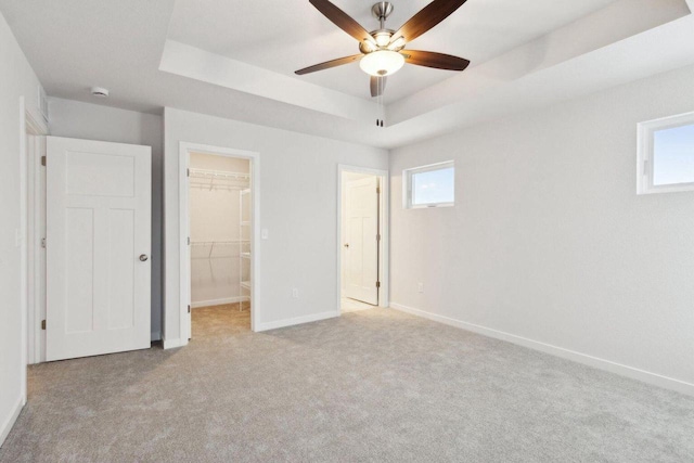 unfurnished bedroom featuring a spacious closet, a closet, light colored carpet, and a raised ceiling