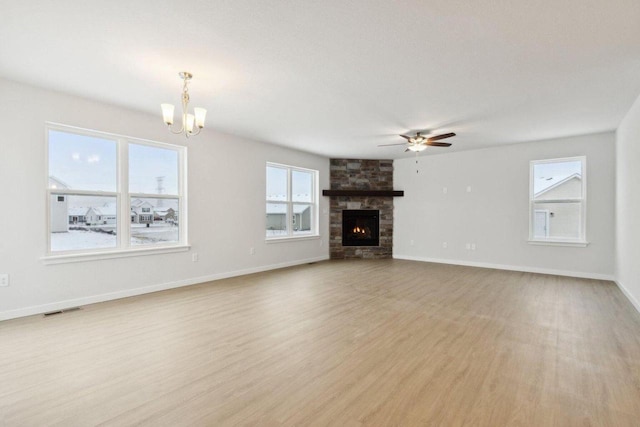 unfurnished living room with ceiling fan with notable chandelier, light hardwood / wood-style flooring, a stone fireplace, and a wealth of natural light