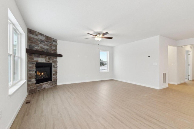 unfurnished living room with light hardwood / wood-style flooring, ceiling fan, and a stone fireplace