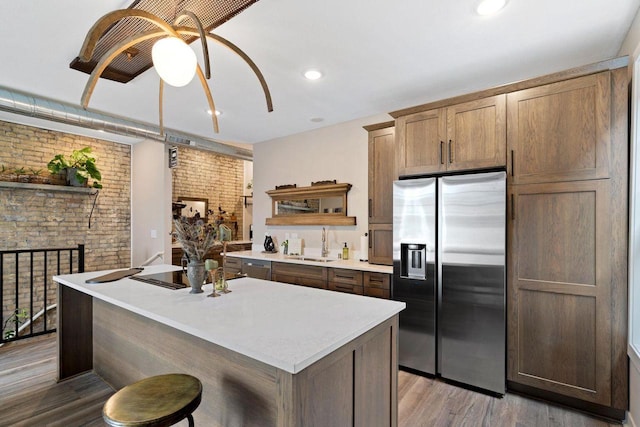 kitchen with appliances with stainless steel finishes, brick wall, an island with sink, light hardwood / wood-style floors, and sink