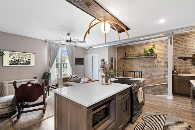 kitchen featuring dark brown cabinets, brick wall, stainless steel appliances, light hardwood / wood-style floors, and a kitchen island