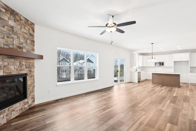 unfurnished living room with ceiling fan, light wood-type flooring, and a stone fireplace