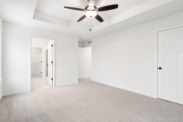 unfurnished bedroom with a tray ceiling, ceiling fan, light carpet, and ensuite bathroom