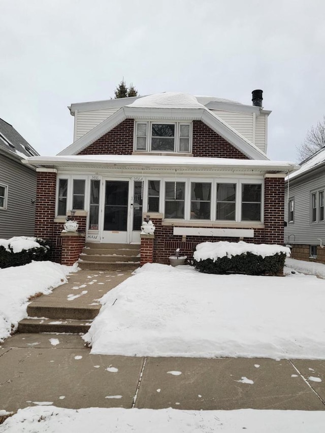 snow covered house with entry steps and brick siding