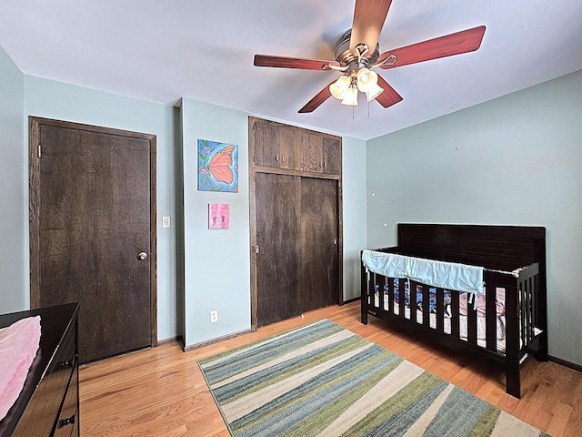 bedroom featuring light wood-type flooring, a closet, a crib, and ceiling fan