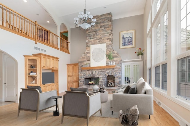 living room with light wood-type flooring, arched walkways, a chandelier, and a stone fireplace