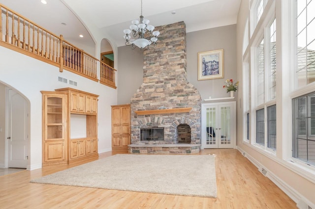 unfurnished living room featuring light wood-style floors, a stone fireplace, an inviting chandelier, and visible vents