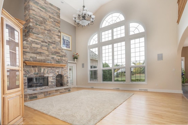 unfurnished living room featuring light wood-type flooring, a towering ceiling, a chandelier, a fireplace, and arched walkways