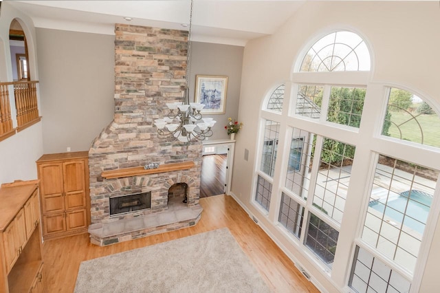 living area with a high ceiling, an inviting chandelier, a stone fireplace, and light wood finished floors