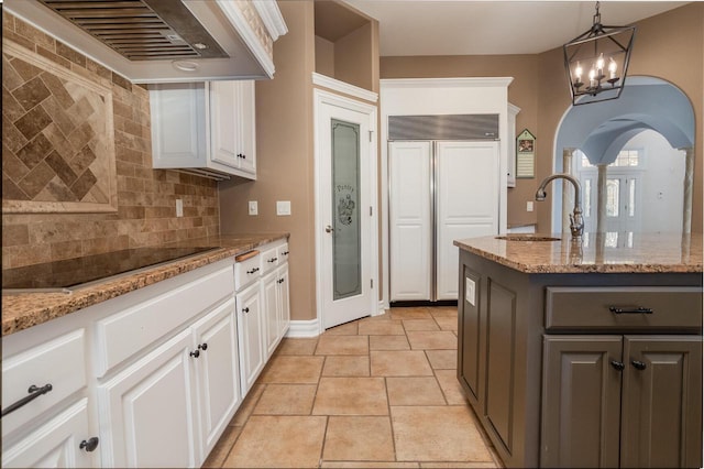 kitchen featuring black electric cooktop, wall chimney exhaust hood, white cabinets, paneled fridge, and a sink