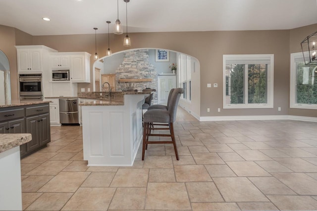 kitchen featuring stainless steel appliances, light stone counters, hanging light fixtures, white cabinetry, and a sink