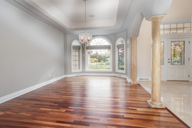 unfurnished dining area featuring dark wood-type flooring, ornate columns, a chandelier, and a tray ceiling