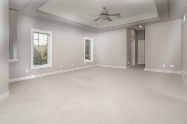 empty room with a ceiling fan, baseboards, light colored carpet, and a tray ceiling