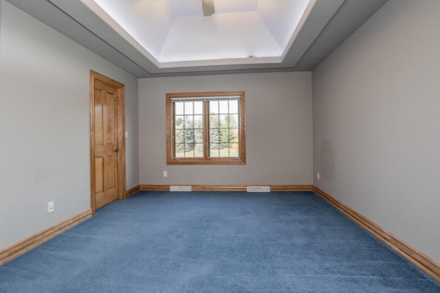 spare room featuring visible vents, dark colored carpet, baseboards, and a tray ceiling